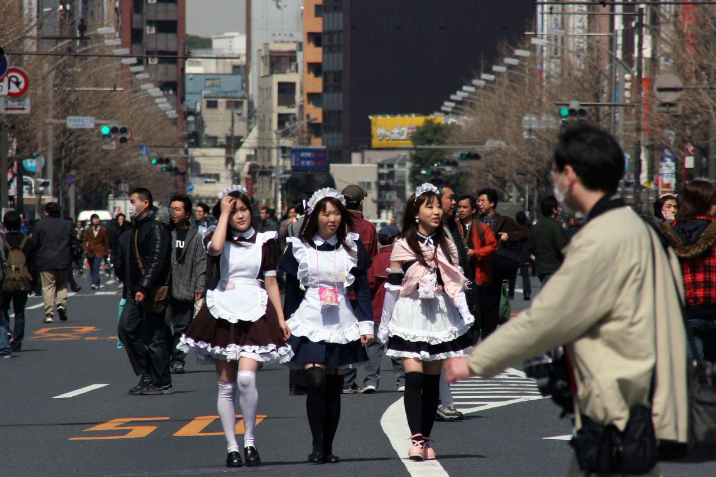 Maid cafe staff in uniform walking through the Akihabara street crowd