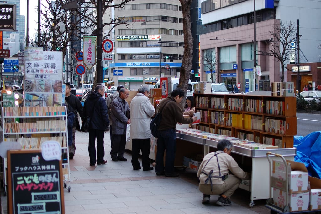 Browsers at bargain book carts outside a used bookstore on a Jimbocho pavement