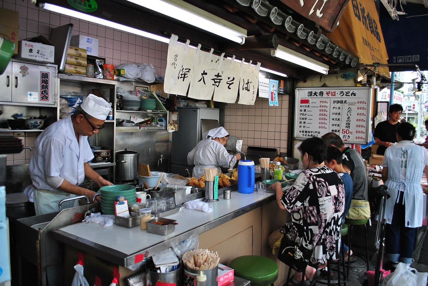 Cooks preparing buckwheat noodles at a busy Jindaiji soba shop counter in Chofu
