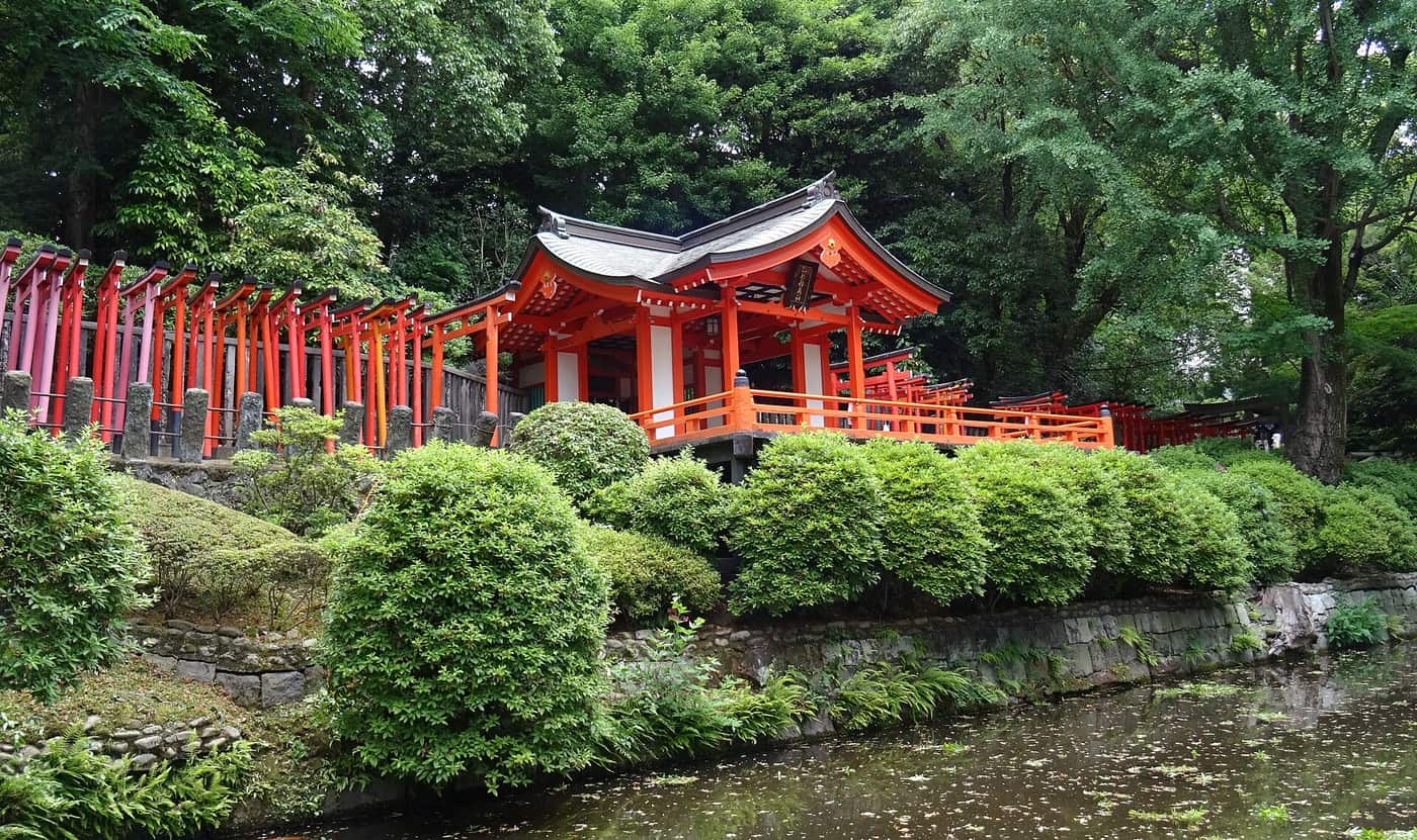 Rows of vermilion torii leading to a small hall on the hillside at Nezu Shrine
