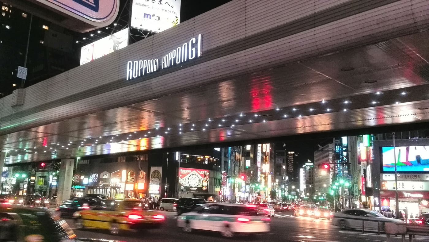 Roppongi Crossing at night with traffic under the lit expressway sign