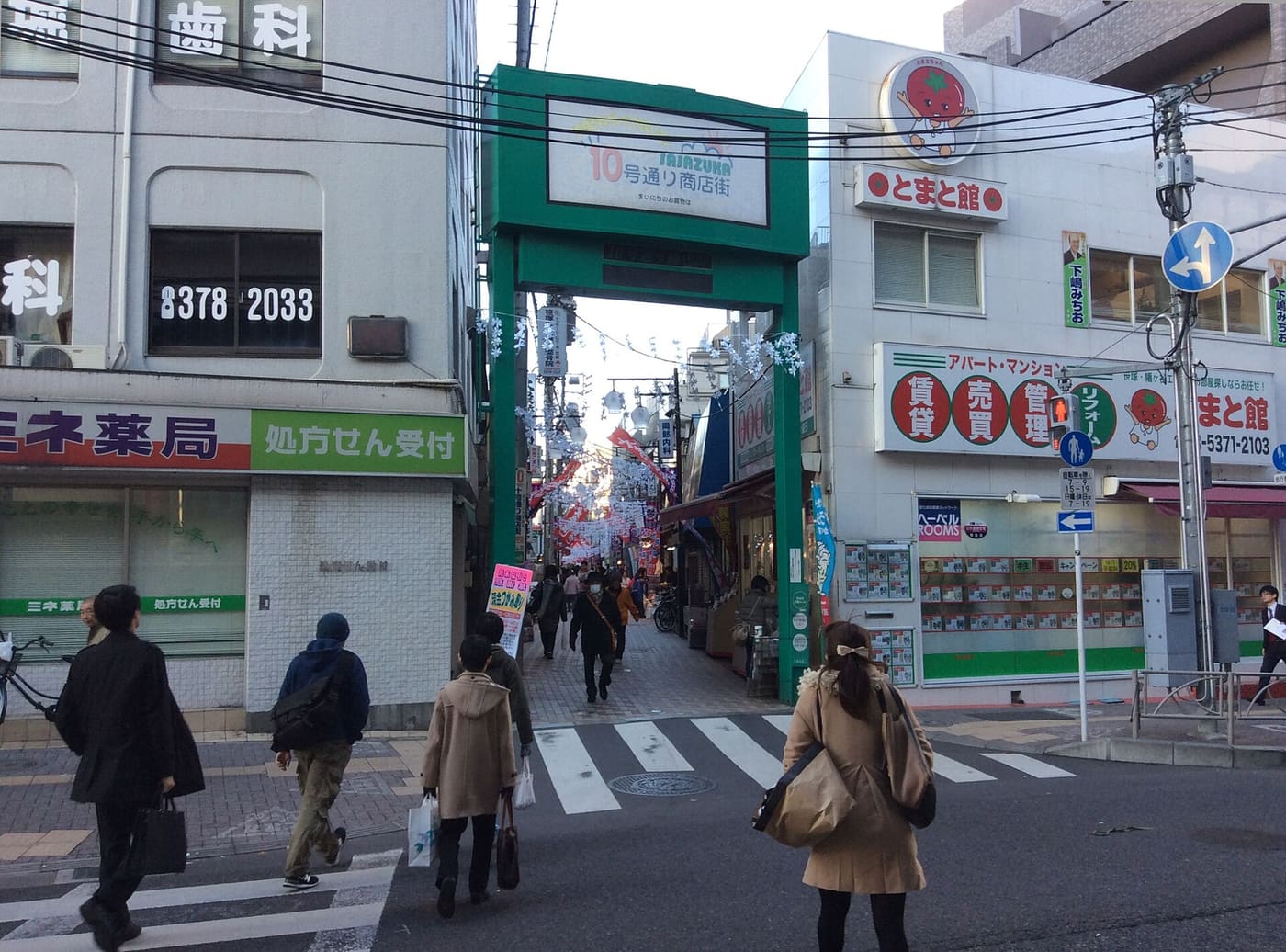 Pedestrians crossing toward the green Jugo-dori shopping street gate in Sasazuka