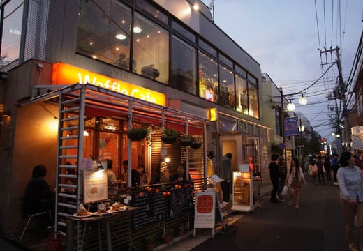 Shimokitazawa street at dusk with a lit cafe terrace and small shops near the station