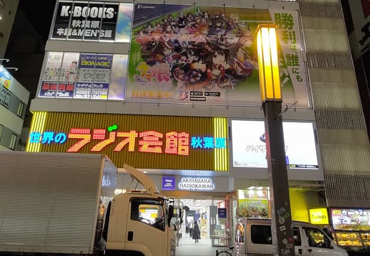Akihabara Radio Kaikan tower glowing with screens and signs at night on Chuo-dori