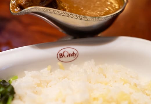 Curry in a gravy boat beside rice topped with melted cheese at Curry Bondy, Jimbocho