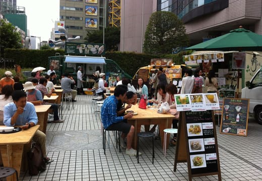 Food stall tables and menu boards on the plaza of the Farmers Market at UNU