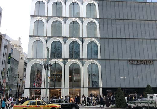 Arched facade of Ginza Six department store along Chuo-dori with a taxi passing