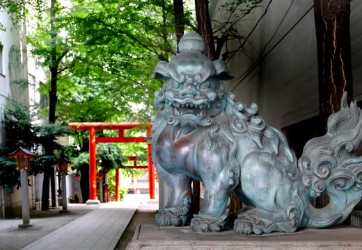 Bronze komainu guardian lion in front of the red torii at Hanazono Shrine, Shinjuku