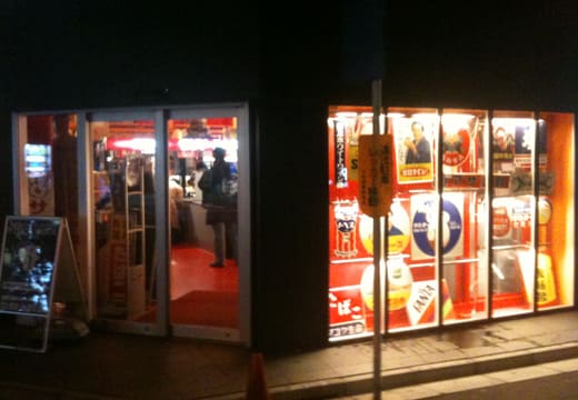 Red-lit ground floor entrance and display windows of Mandarake Complex at night, Akihabara