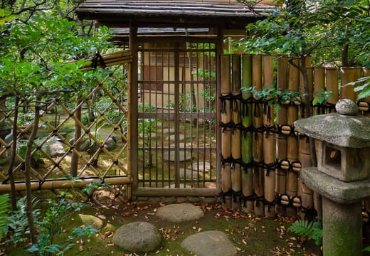 Bamboo gate and stone lantern along a path in the Nezu Museum garden
