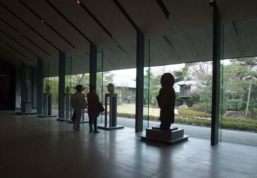 Visitors in the lobby of the Nezu Museum with a stone Buddha before garden windows