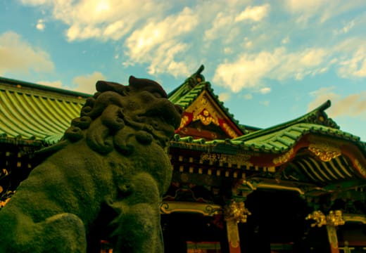 Moss-green komainu guardian dog in front of the ornate roofs of Nezu Shrine