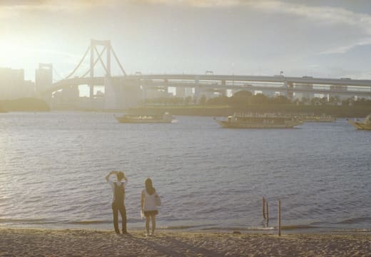 Visitors on the sandy beach of Odaiba Seaside Park facing Rainbow Bridge at golden hour