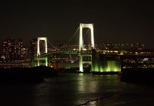 Rainbow Bridge lit up at night across the water from Odaiba Seaside Park
