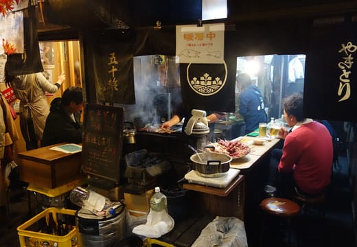 Cook tending a yakitori grill behind the counter of an Omoide Yokocho stall