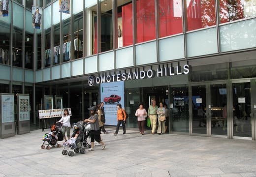 Entrance of Omotesando Hills with its name on the glass facade and shoppers outside