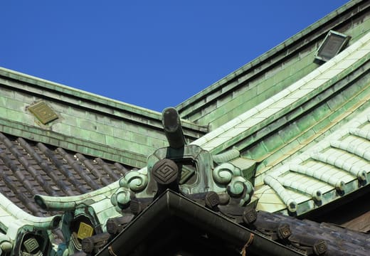 Green copper roof and carved ridge ends of a hall at Shibamata Taishakuten against blue sky