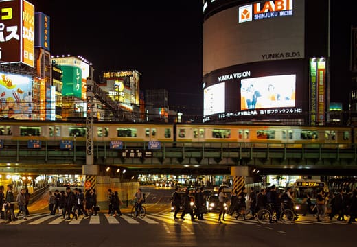 Yamanote Line train passing over a busy crossing in Shinjuku at night under neon signs