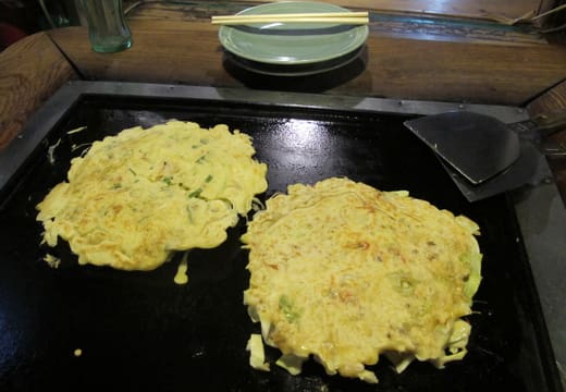 Two okonomiyaki pancakes cooking on the table griddle at Sometaro in Asakusa