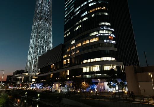 Tokyo Skytree lit in blue and purple at night beside a residential tower