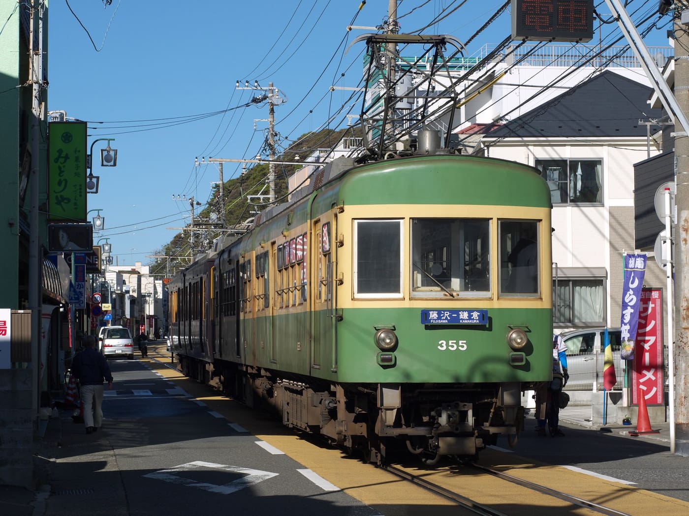 A green Enoden tram running between houses on the line to Enoshima