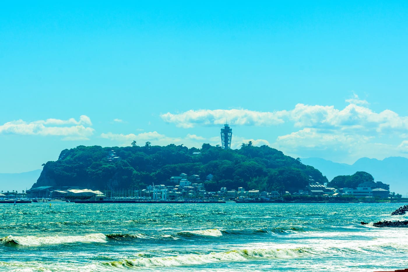 Enoshima island and its lighthouse tower seen across the beach and surf