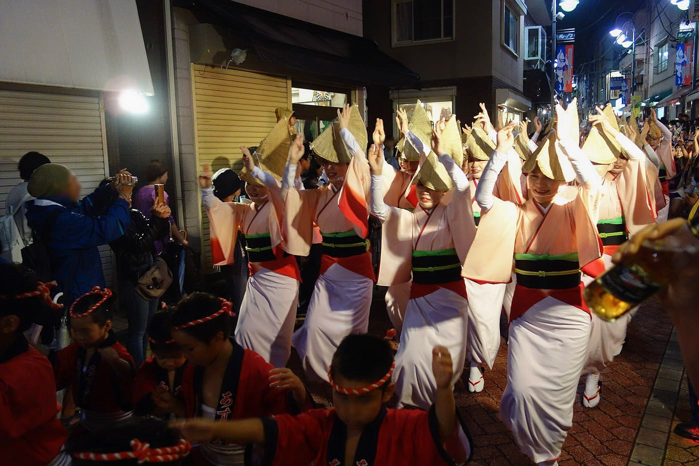 An Awa Odori troupe in white yukata and straw hats dancing through Koenji at dusk