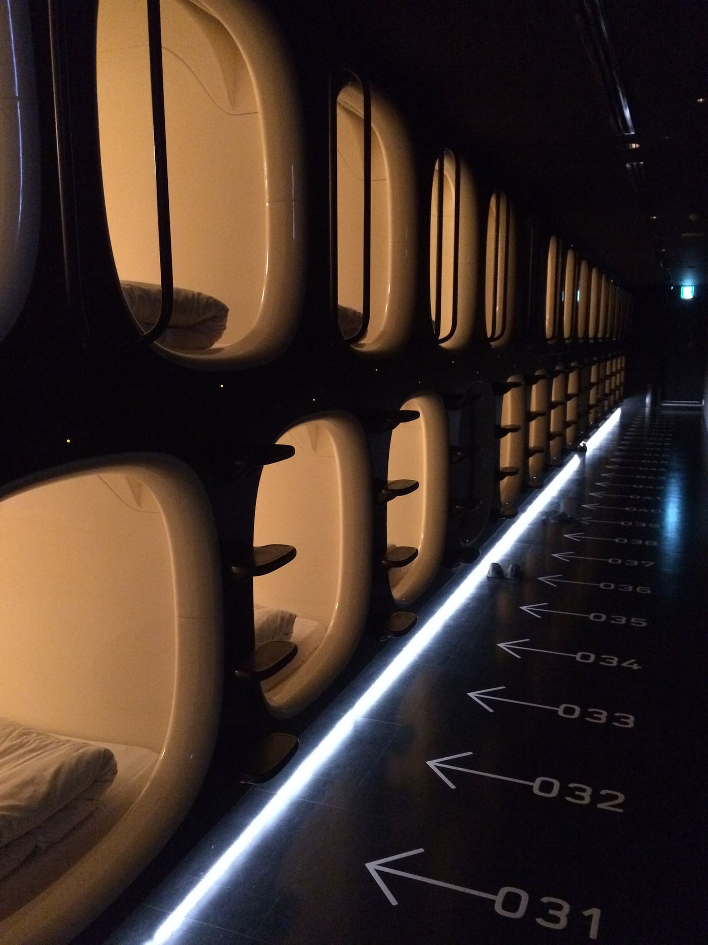 The dim sleeping hall of a modern pod hotel in Tokyo with rows of capsules