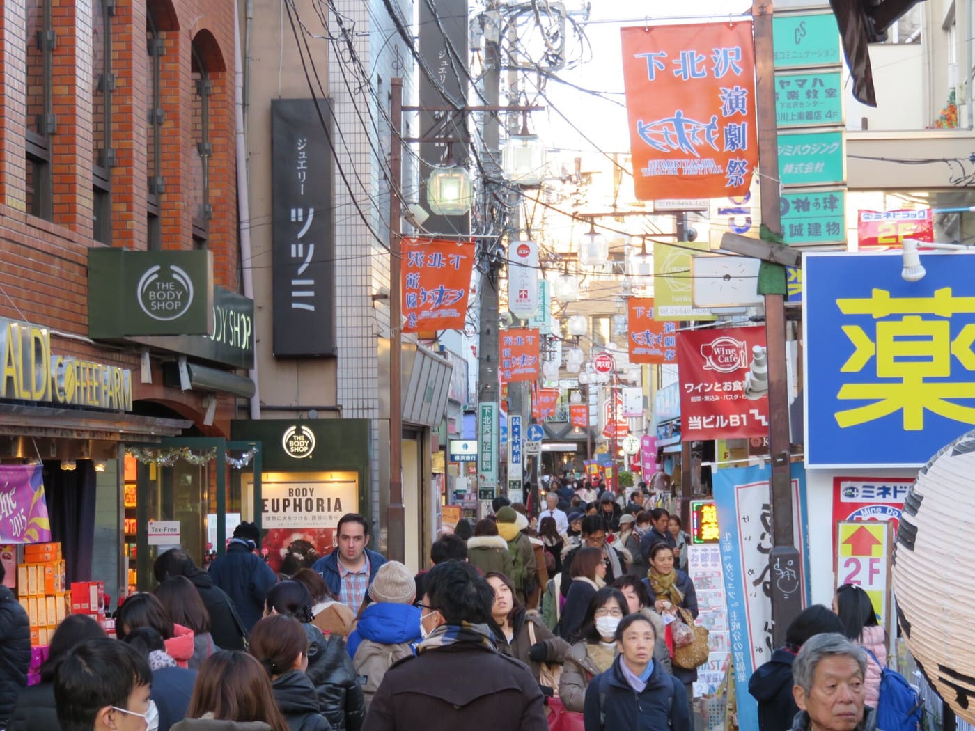 Shoppers on a narrow shopping street lined with signs in Shimokitazawa