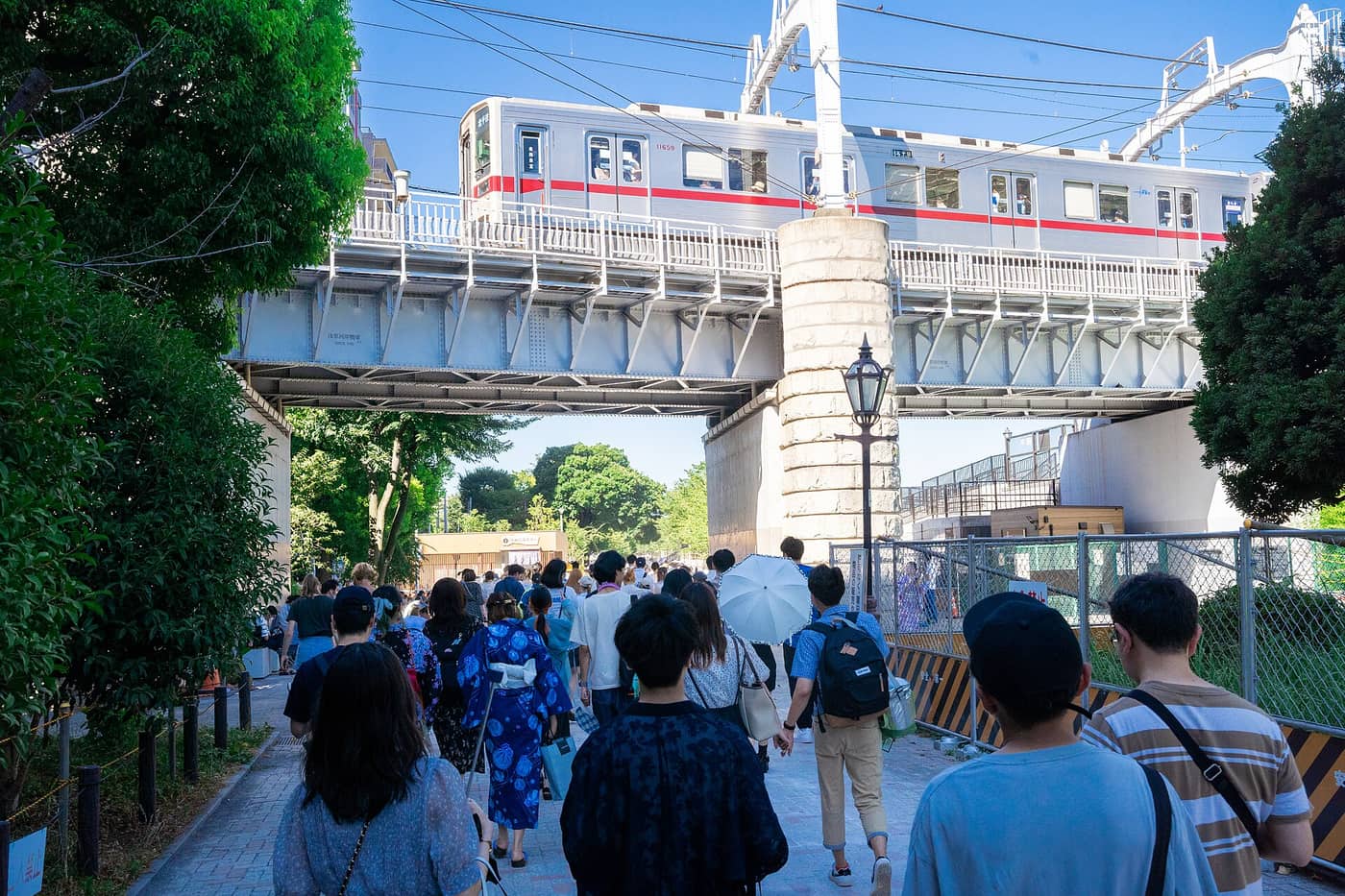 Crowds in yukata walking the Sumida riverside path under the railway bridge on fireworks day