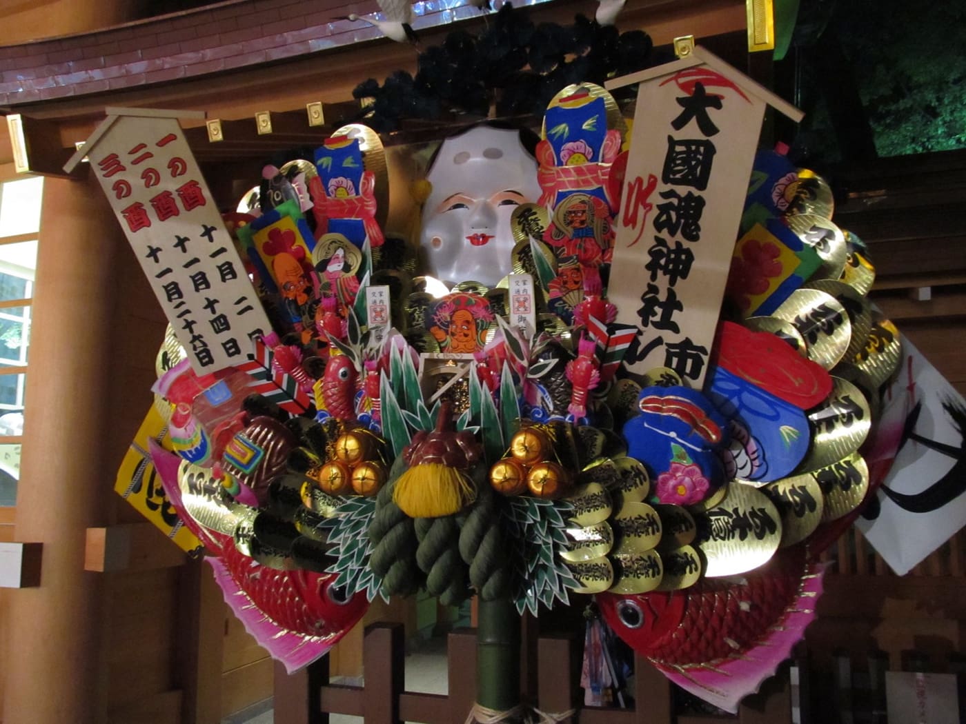 A large kumade decorated with an Okame mask, rice bales and lucky charms