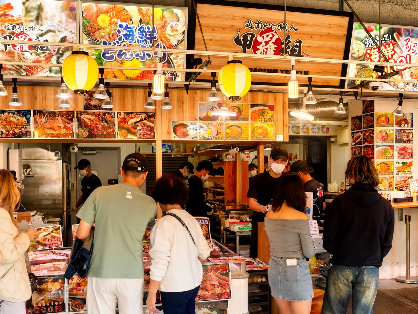 Shoppers ordering seafood beneath red lanterns at a Tsukiji Outer Market stall