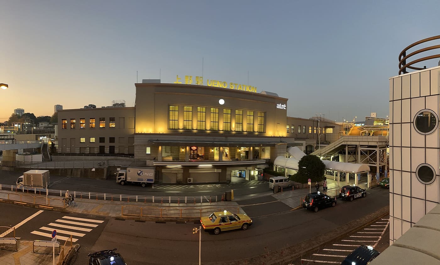 Travellers crossing the busy forecourt of JR Ueno Station in late autumn