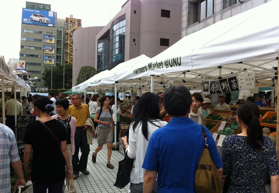 Shoppers browsing white-tented produce stalls at the Farmers Market at UNU in Aoyama