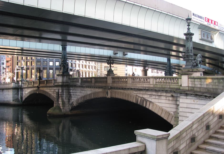 Twin stone arches of Nihonbashi Bridge over the river beneath the elevated expressway