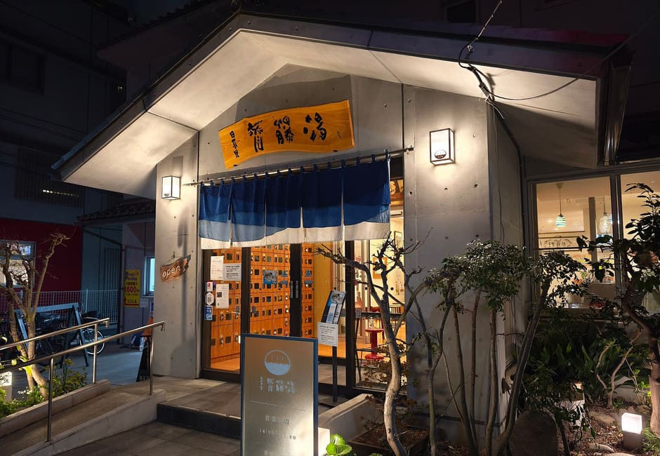 Lit entrance of Saitoyu sento with its noren and wooden sign at night near Nippori station