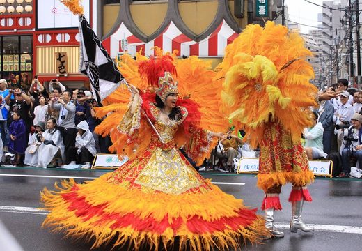 A samba dancer in an orange feathered costume parading through Asakusa at the carnival