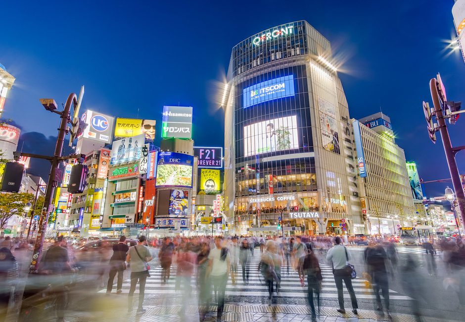 La foule traverse le carrefour de Shibuya à l’heure bleue, sous les écrans de QFront