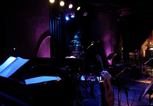 Stage of Minami-Aoyama Mandala set with piano and guitars under purple light