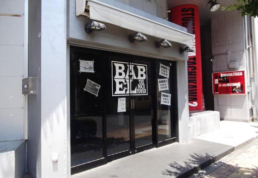 Black entrance doors and BABEL logo of the Tachikawa live house on a sunny street