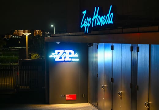 Blue neon Zepp Haneda sign above the hall's entrance at night by Haneda Airport